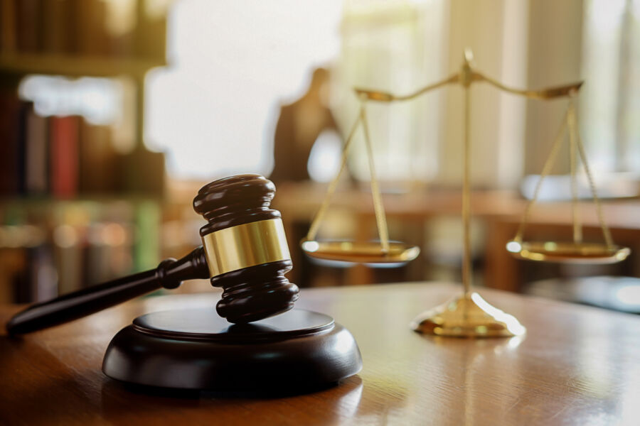 Judge's gavel prominently displayed, while Justice lawyers collaborate in a team meeting at a law firm behind it