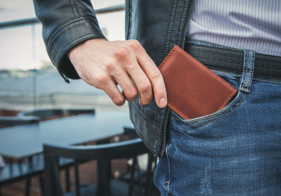 Close-up of a man retrieving a brown leather wallet from his jeans pocket