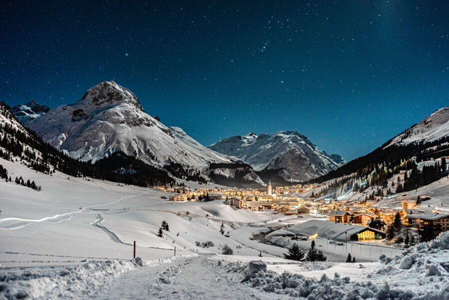 Nighttime view of snowy mountains in Lech, Austria, with a tranquil atmosphere under the starry sky