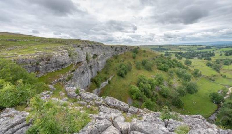 Limestone escarpment overlooking lush green valley in Malham Cove