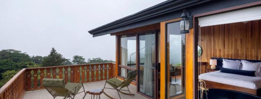 Rustic cabin balcony with wooden furniture, forest view, and cozy interior.