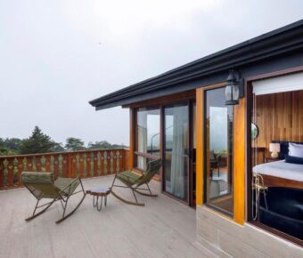 Rustic cabin balcony with wooden furniture, forest view, and cozy interior.