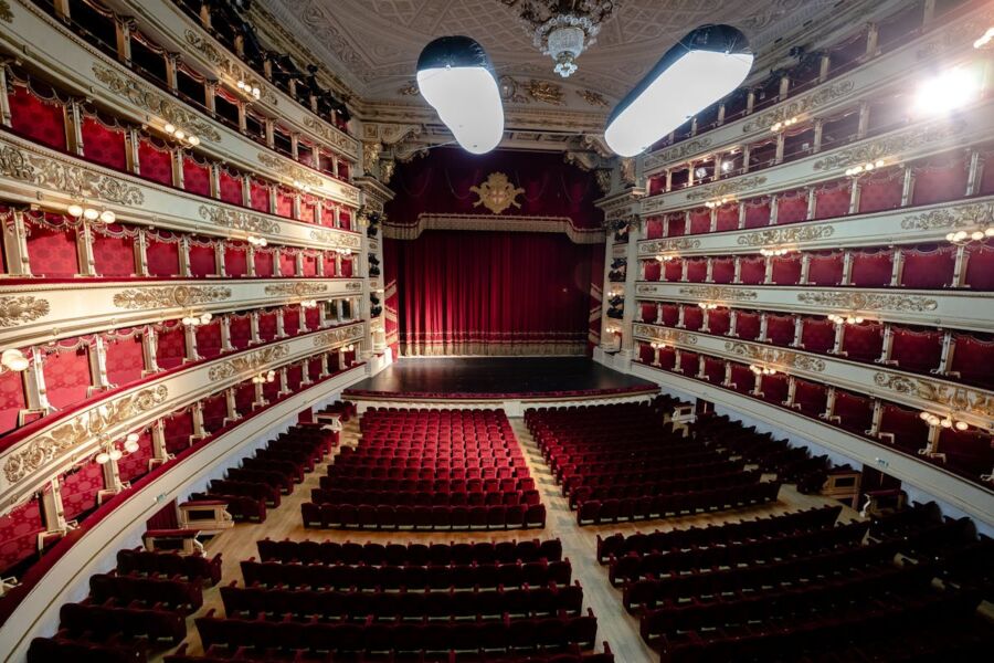 Opulent theater interior with red velvet seats, golden embellishments, and grand stage curtain.