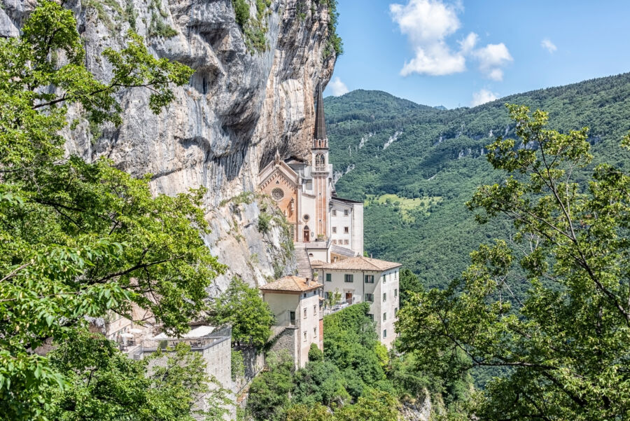 The Sanctuary of Madonna Della Corona, perched on a cliff in Italy, features remarkable architecture against a scenic mountain backdrop