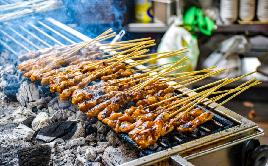 Grilled chicken satay skewers cooking over charcoal, showcasing a delicious Malaysian dish