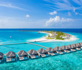 Aerial view of a luxury tropical resort in the Maldives, featuring water villas and stunning beach scenery