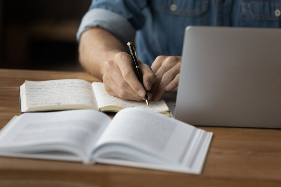 Close-up of a male student taking handwritten notes in a notebook while studying intently