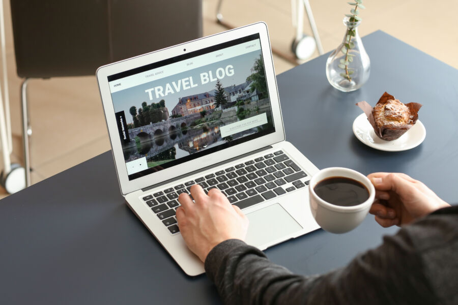 Close-up of a male travel blogger working on his laptop with a cup of coffee