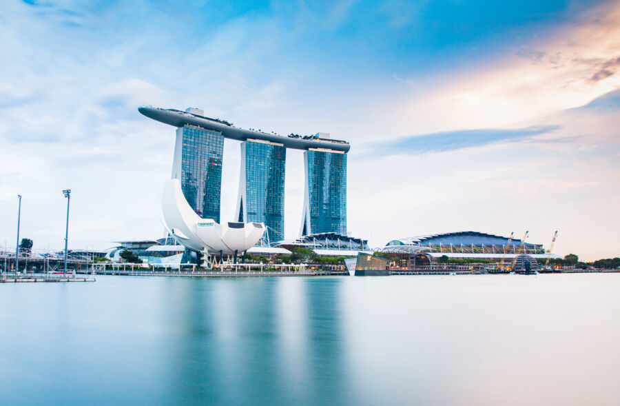 Night view of Singapore's Marina Bay skyline featuring Marina Bay Sands, ArtScience Museum, and illuminated tourist boats