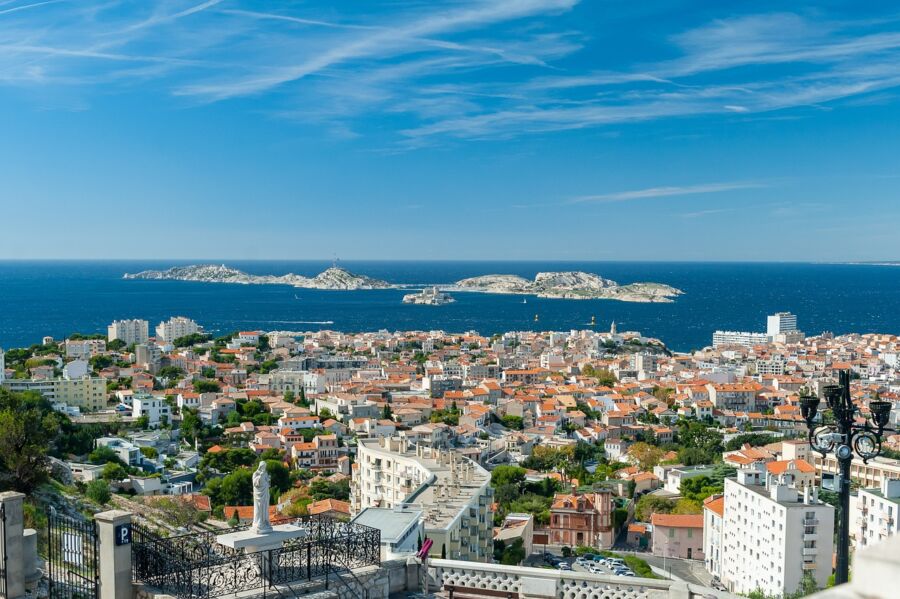 Panoramic view of Marseille coastline with terracotta roofs, blue sea, and a white statue.