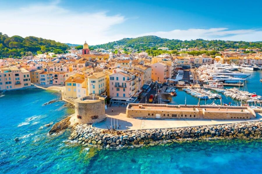 Aerial view of vibrant Mediterranean coastal town with yachts, waterfront, and historical architecture.