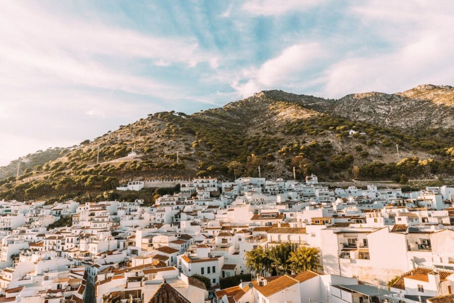 Charming Mediterranean village with white buildings, red roofs, and lush mountains under a golden sky.