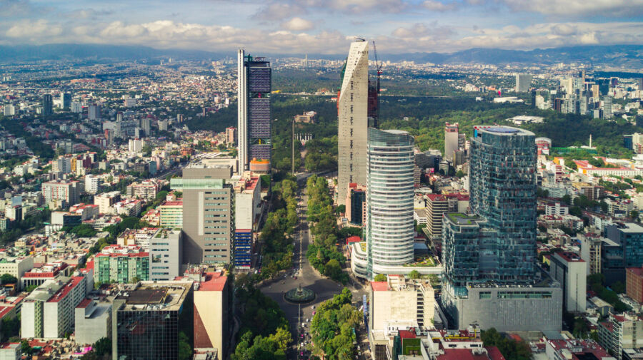 The skyline of Mexico City features a mix of historic and contemporary buildings under a colorful sky at dusk