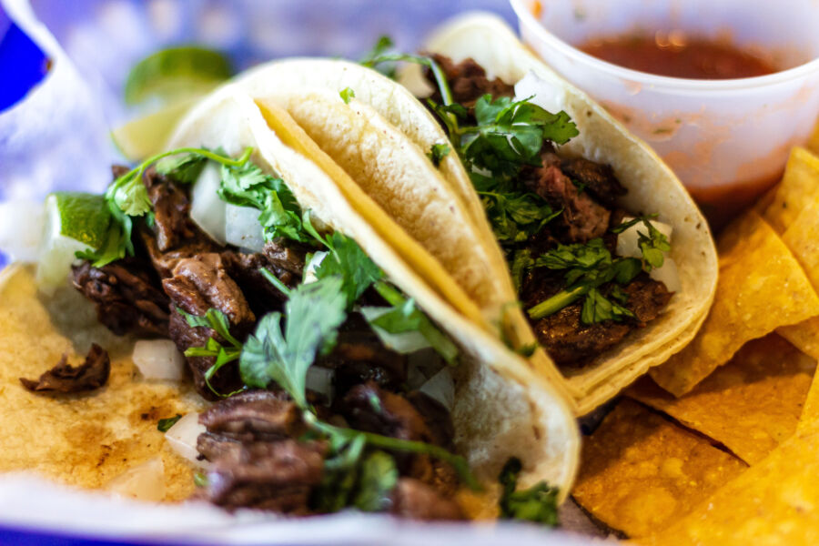 Two carne asada tacos topped with cilantro and onion, served on warm corn tortillas