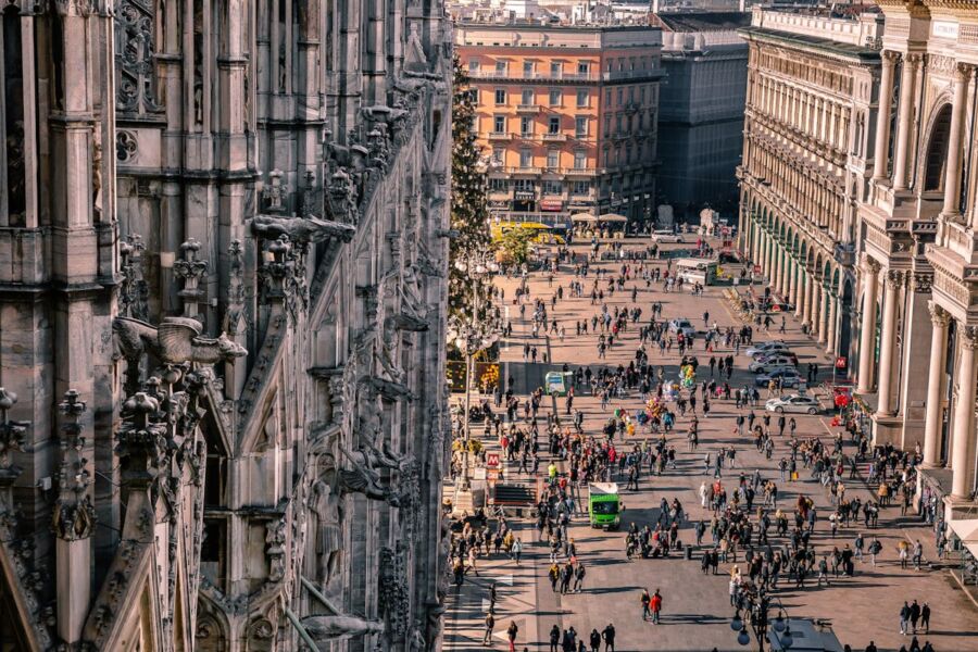 Aerial view of bustling Milan square with gothic cathedral, modern buildings, and sunset.