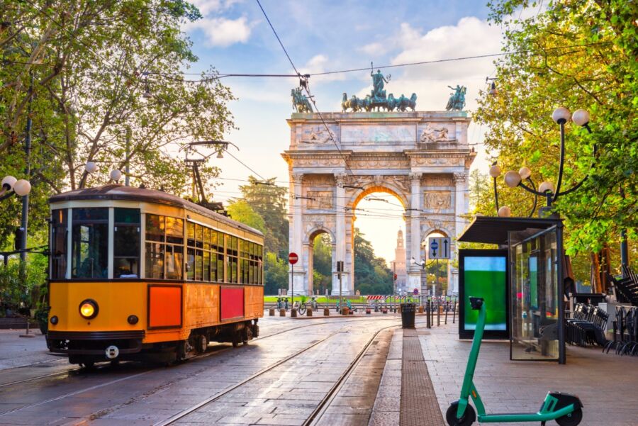 Tram and scooters near Porta Sempione Arch in Milan, showcasing urban transport and vibrant city life