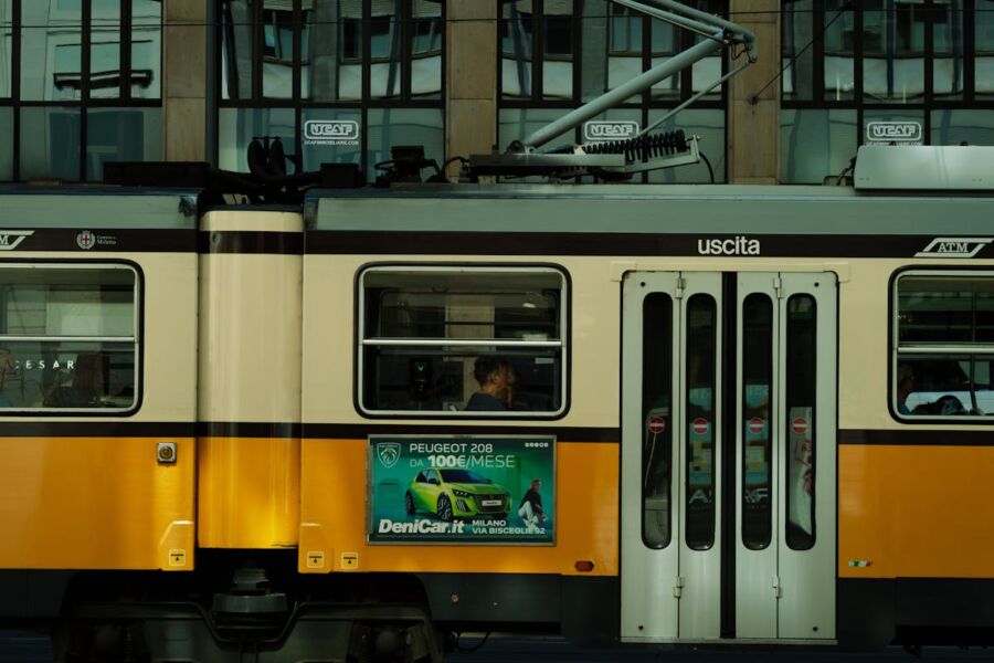 Side view of a yellow tram with Peugeot ad in modern Italian cityscape.