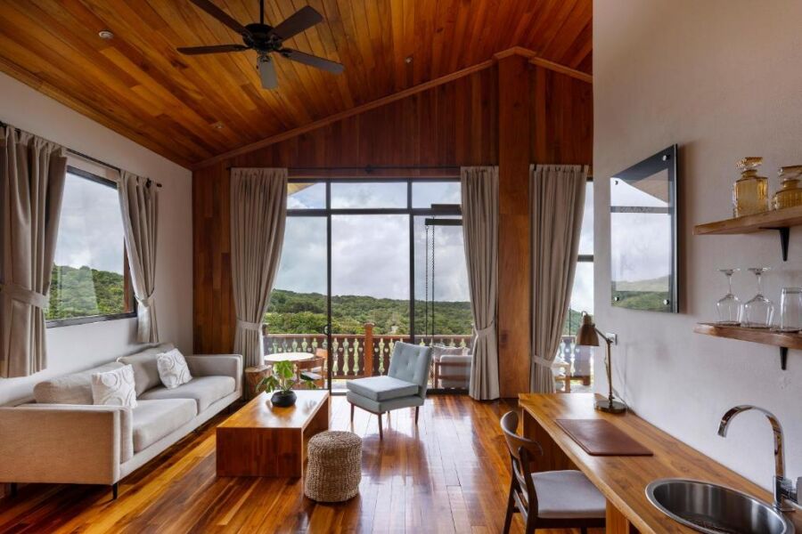 Modern living room with wooden ceiling, cozy sofa, natural light, and lush outdoor view.