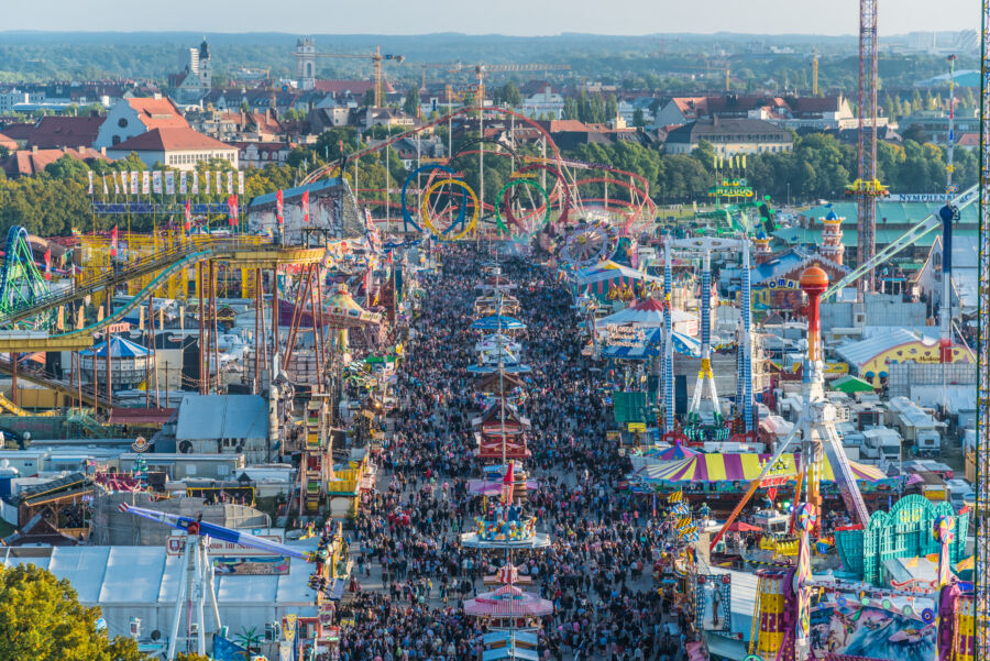 Aerial view of a large crowd at Oktoberfest, with colorful tents and attractions visible, taken from St. Paul Cathedral in Munich