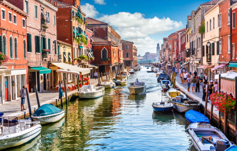 Scenic view of Murano Island's canal in Venice, showcasing colorful houses and boats amidst a serene Italian landscape