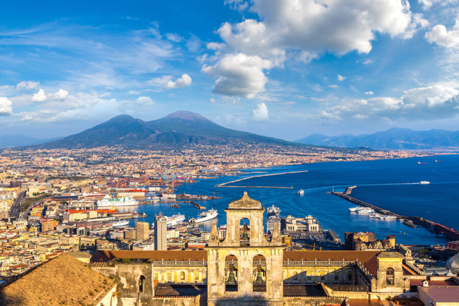 Naples city skyline featuring colorful buildings, with the iconic Mount Vesuvius rising majestically behind it