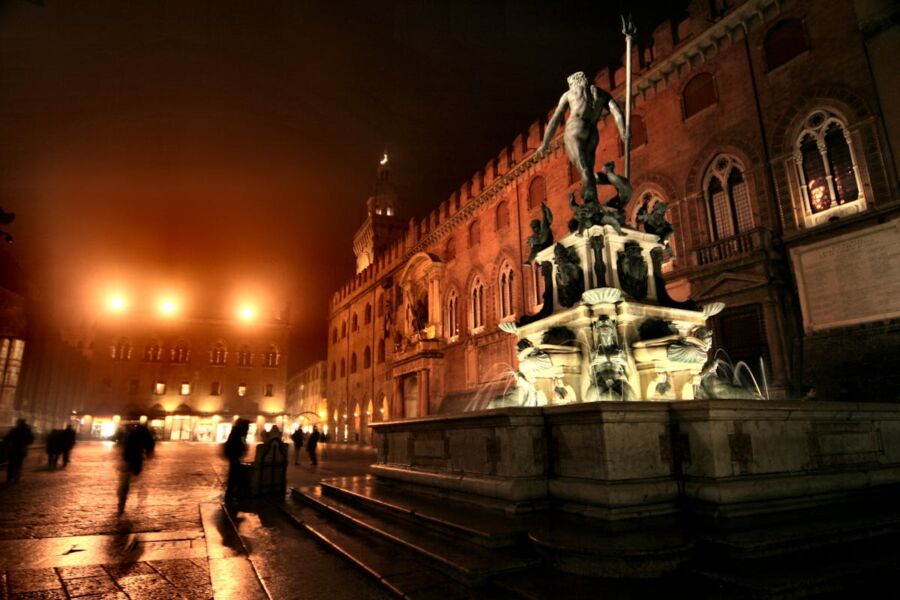 Neptune fountain at historic European square illuminated at night with architectural highlights.