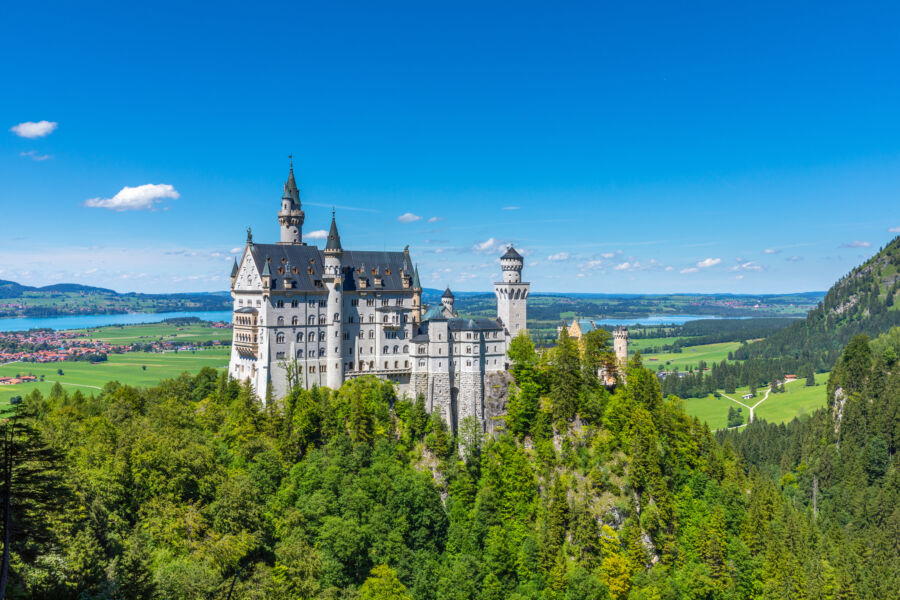 Scenic view of Neuschwanstein Castle in the Bavarian Alps, surrounded by lush greenery and a clear blue sky