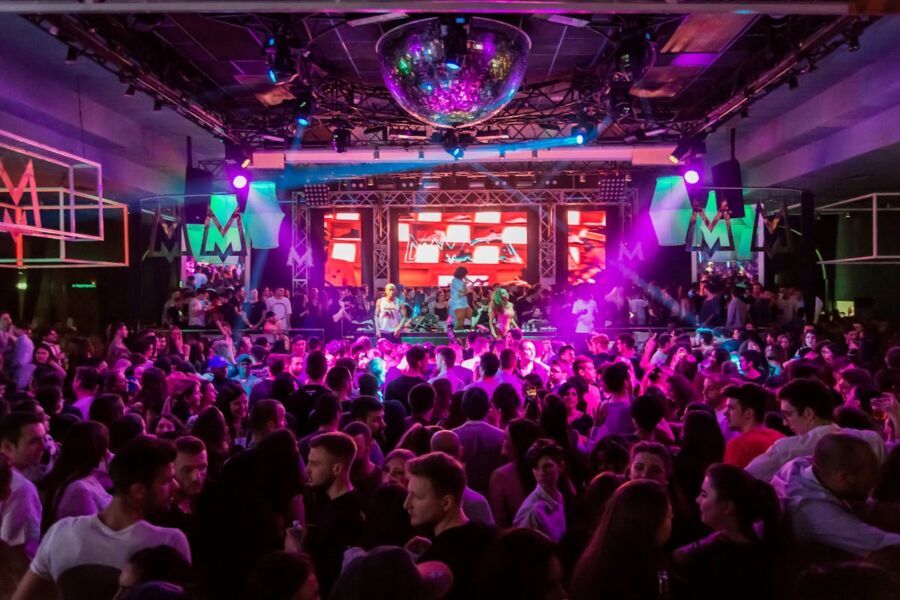 Vibrant nightclub scene with diverse crowd, colorful lights, and festive atmosphere.