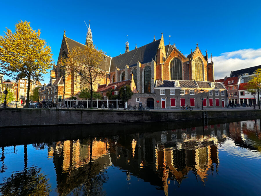 Oude Kerk reflected in a canal on a spring day in Amsterdam, showcasing the historic architecture and vibrant surroundings