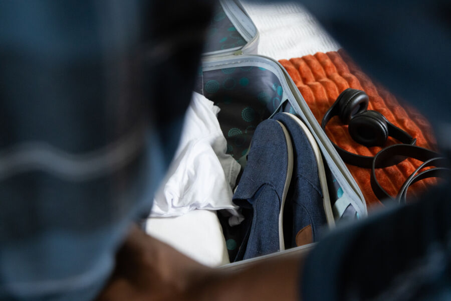 Man packing a suitcase with shoes and headphones, preparing for holiday travel at home