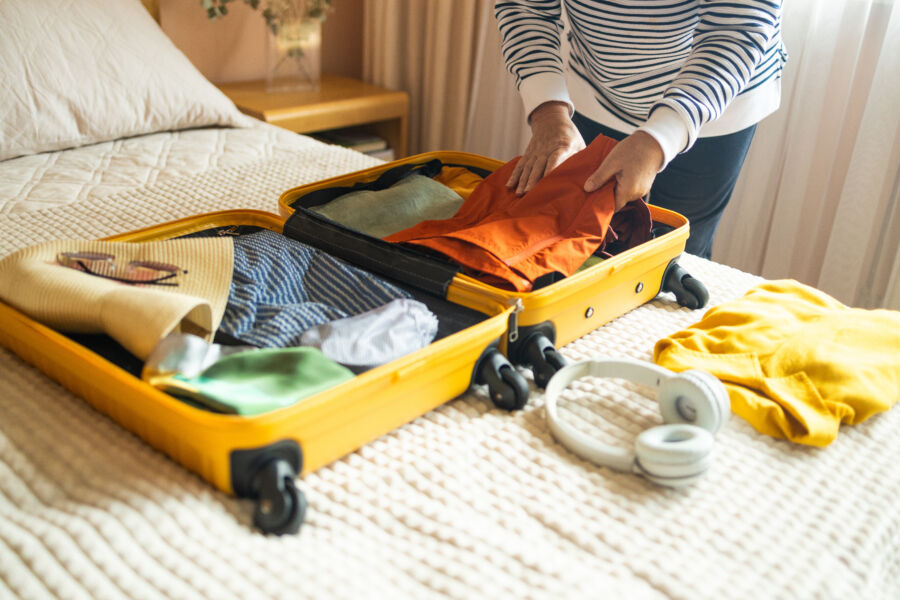 Woman organizing travel clothes on a bed, preparing a suitcase for an upcoming vacation journey