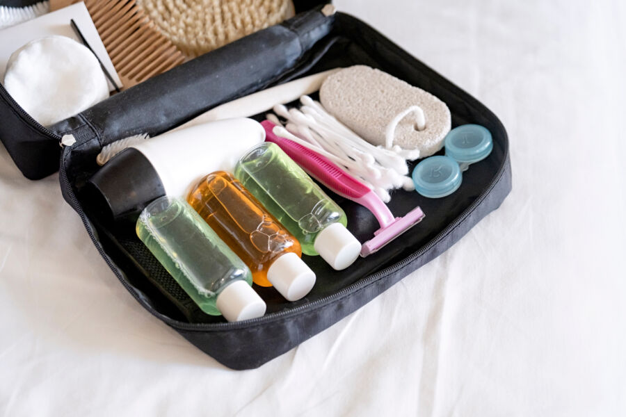 Travel cosmetics kit with bottles, brushes, and toiletries arranged neatly on a bed, ready for packing