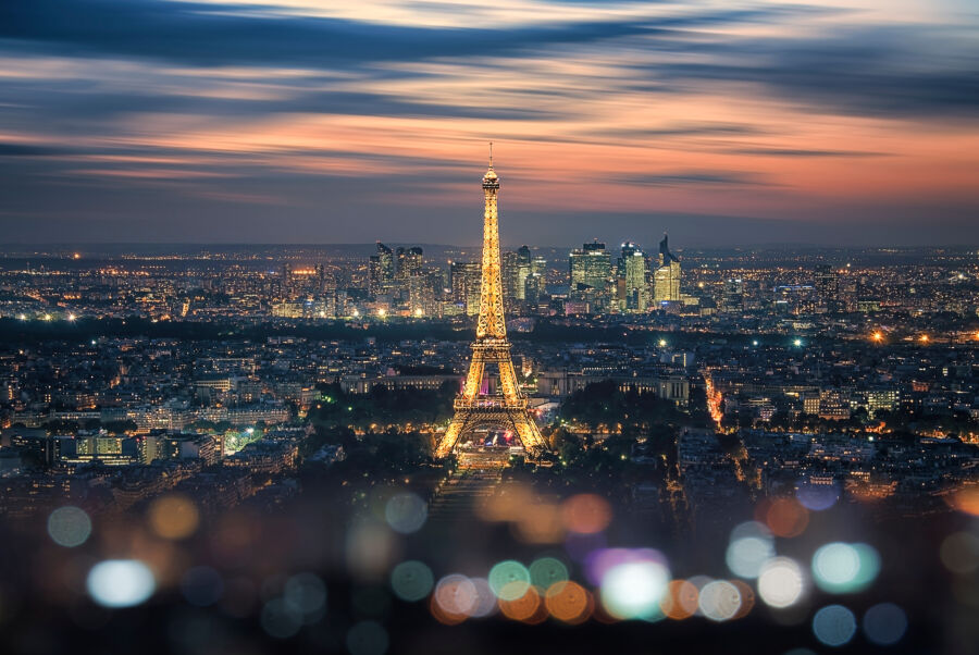 Evening view of Paris featuring the illuminated Eiffel Tower and La Defense business district, showcasing vibrant city lights