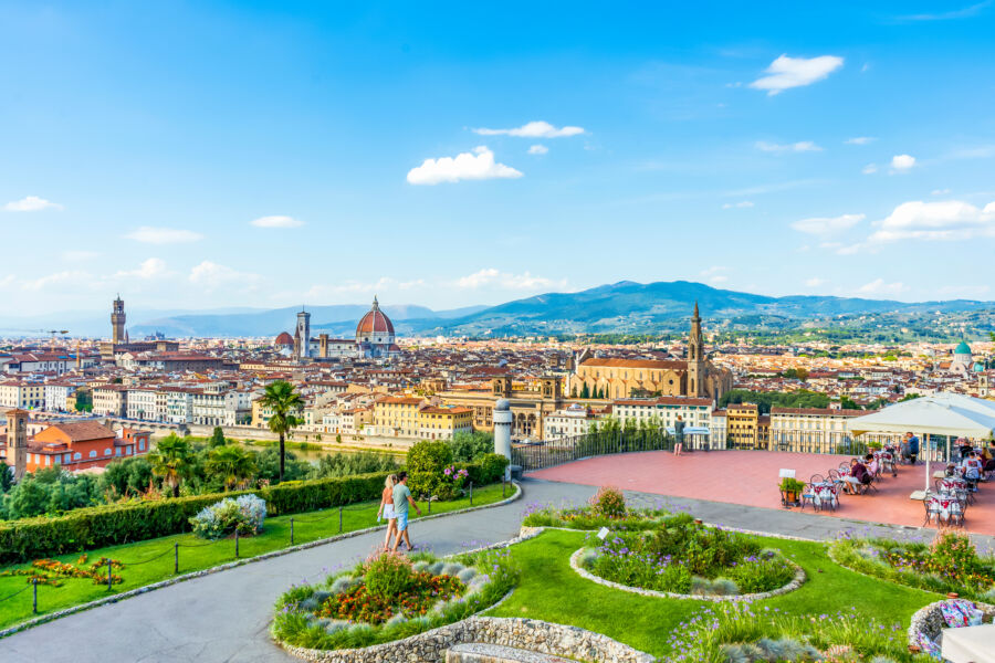 Scenic view of Florence from Piazzale Michelangelo, featuring the cathedral, blue sky, and a couple walking in Tuscany, Italy