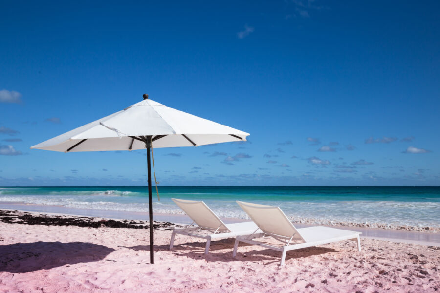 Picturesque scene of a Pink Sands Beach in the Bahamas, complete with a beach umbrella and soft waves for a perfect getaway