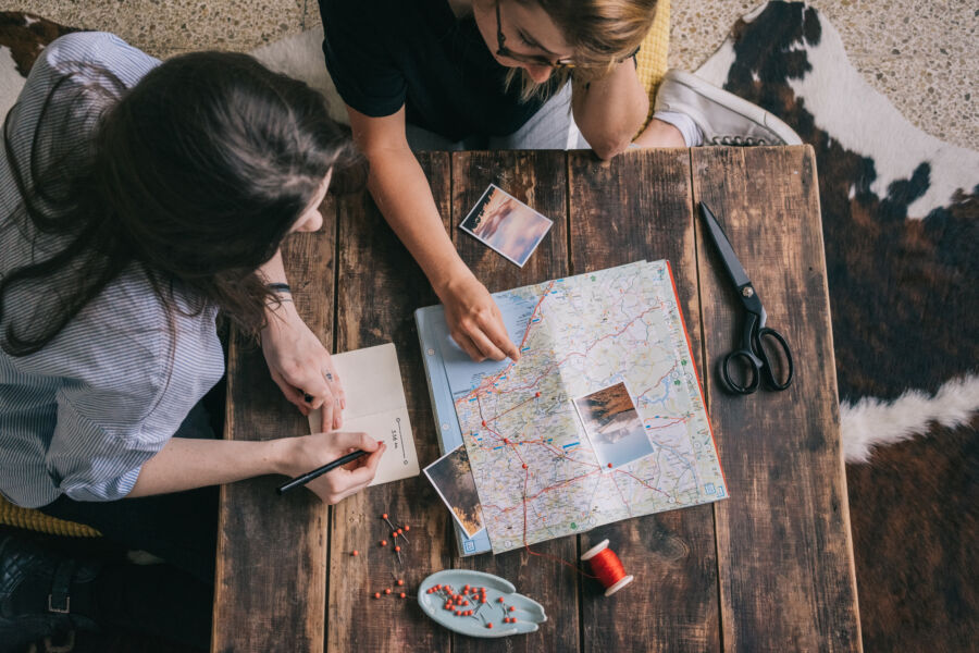 Person studying a map while planning a trip, surrounded by travel essentials and a notebook for notes