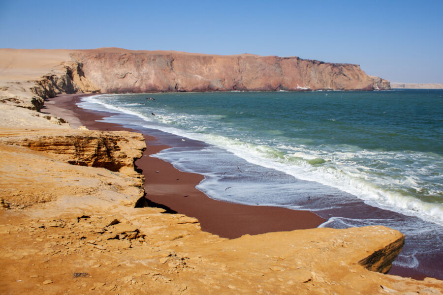 The picturesque red beach in Paracas Nature Reserve, featuring striking red sands meeting the clear waters of the coast