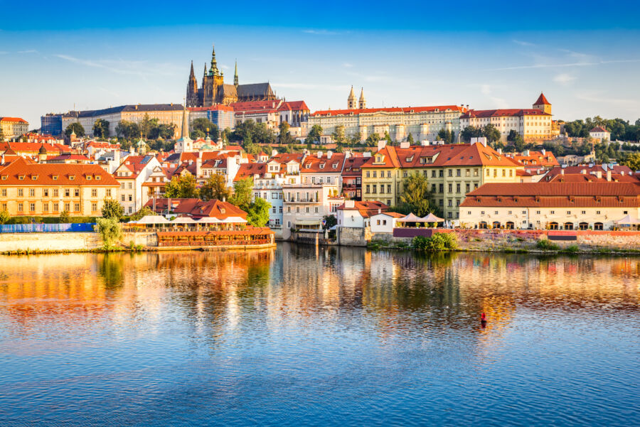 The majestic Prague Castle dominates the skyline, surrounded by the vibrant cityscape of Prague under a sunny sky