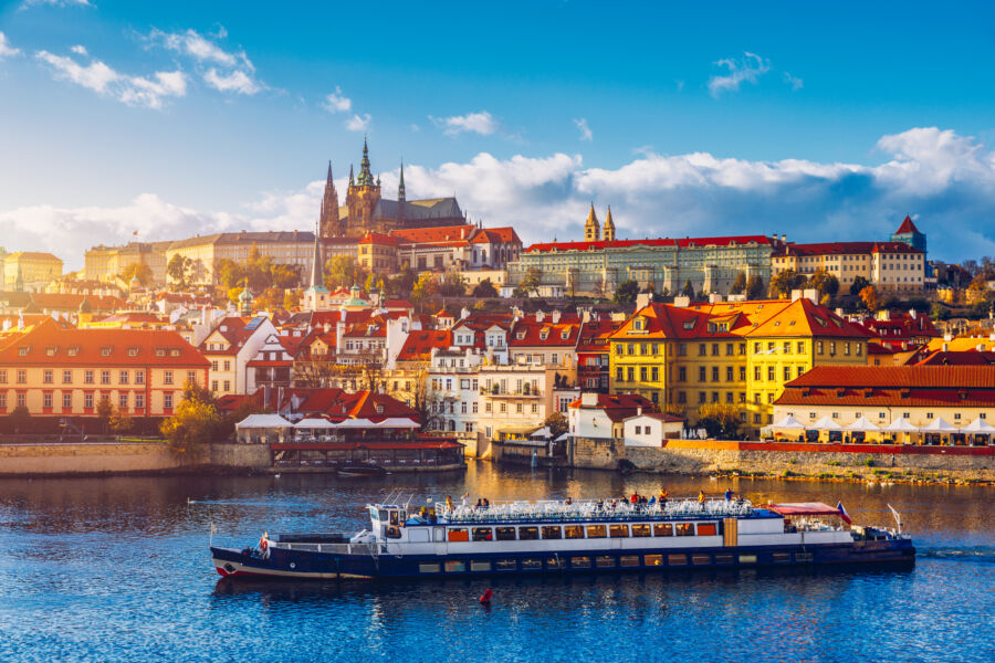 Scenic view of Prague Castle and Charles Bridge over the Vltava River, featuring boats cruising in the heart of Czechia