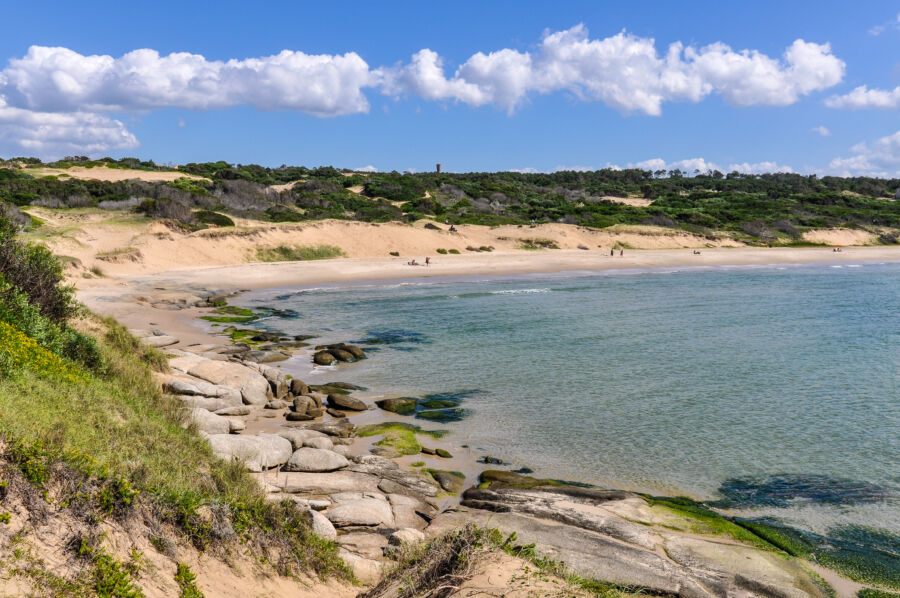 Scenic beach view of Punta del Diablo, Uruguay, featuring golden sands and gentle waves under a clear blue sky