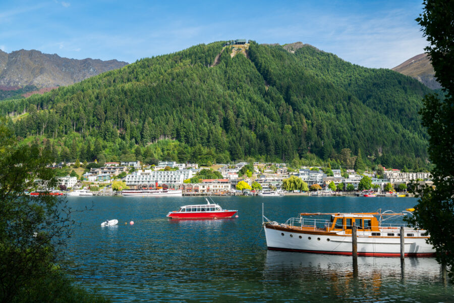 Beautiful lakefront in Queenstown, New Zealand, showcasing cozy homes and boats with picturesque mountain views