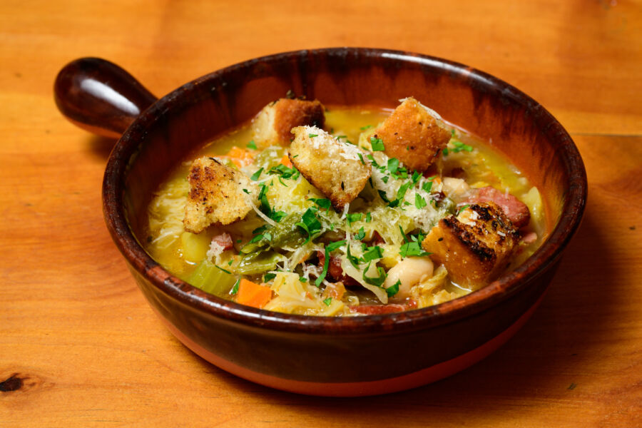 Ribollita soup in a terracotta bowl, featuring Tuscan bread, beans, and an assortment of vibrant winter vegetables