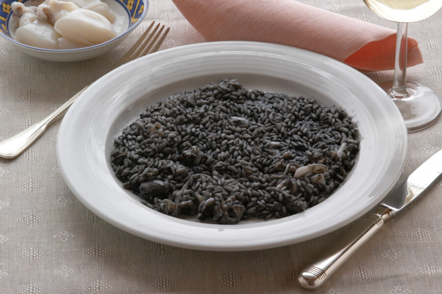 Close-up of a plate of risotto al nero di seppia, showcasing its rich black color and garnished with fresh herbs