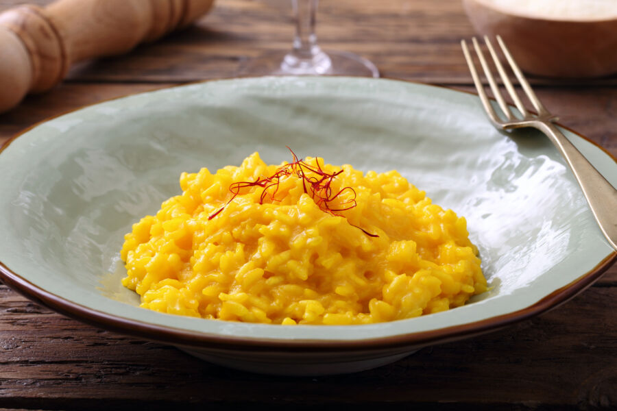 Close-up of risotto alla Milanese on a white plate, garnished and accompanied by a fork, showcasing its creamy texture