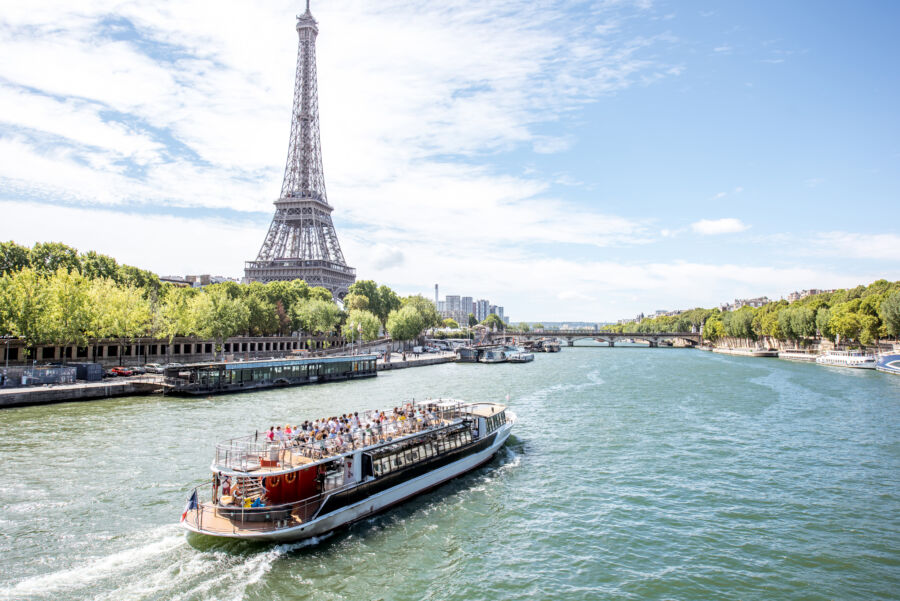 Scenic view of the Eiffel Tower and Seine River, featuring a tourist boat gliding through the picturesque Paris landscape