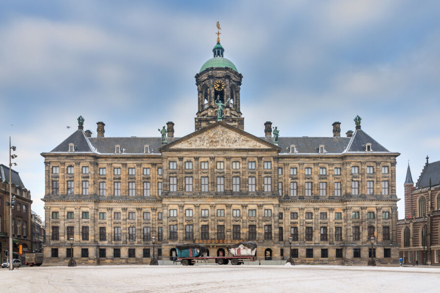 Scenic view of the Royal Palace at Dam Square, Amsterdam, with snow blanketing the ground and bright blue skies.