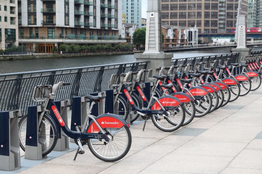 Row of Santander Cycles bike hire station in Canary Wharf, London, with several bicycles lined up for rental.
