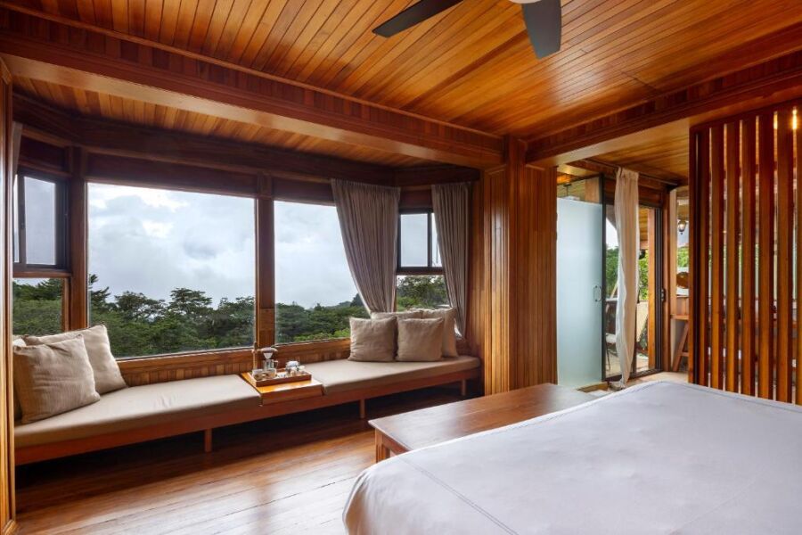 Cozy wood-themed bedroom with panoramic windows and lush outdoor view.