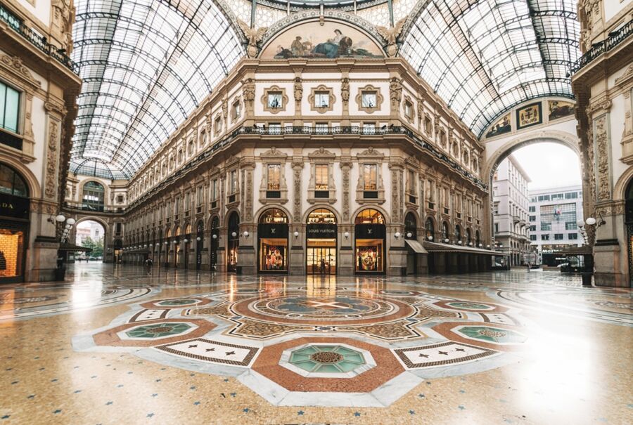 Elegant shopping arcade interior with vaulted glass ceiling, luxury stores, and mosaic flooring.