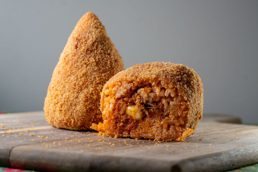 Close-up of Sicilian Arancini on a wooden board, showcasing the exposed filling and golden, crispy exterior